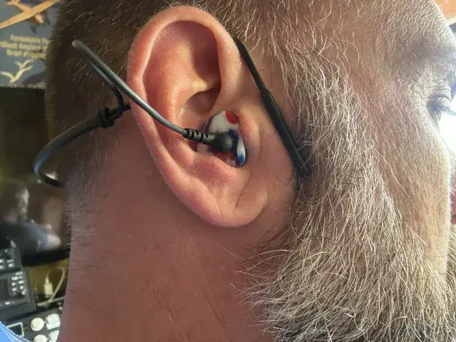 Close-up of a red, white and blue custom Clarity Aloft adapter worn in the ear